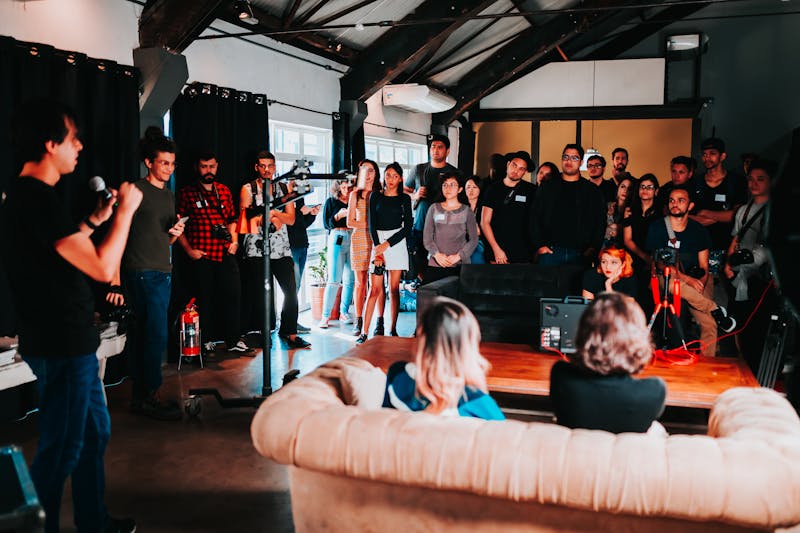 Speaker with a microphone addresses a standing crowd in a warehouse event space
