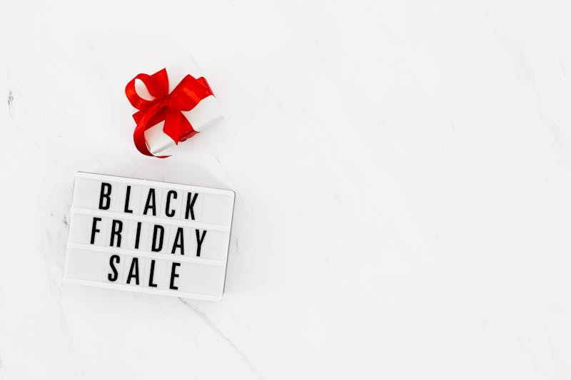 Light box sign reading "Black Friday sale" beside a gift with a red ribbon, on white marble