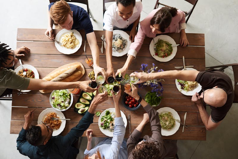 Overhead view of friends raising drinks over a wooden table of shared dishes
